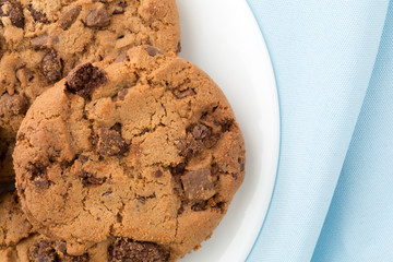 Top view of a plate of gourmet milk chocolate chip cookies with a blue napkin.