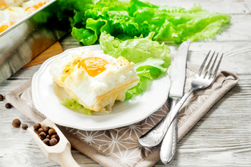 
breakfast or lunch , air , beaten egg and baked in the oven , with lettuce and herbs on a white wooden background