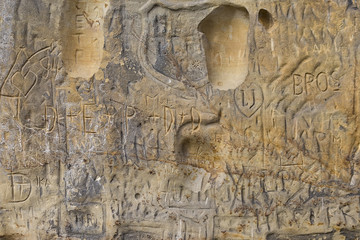Old sandstone wall or rock with old writing of many nameless peo