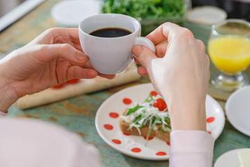 Womans hands holding up a cup of coffee during breakfast