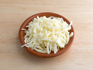 Pizza cheese in small bowl illuminated with window light on a wood table top.