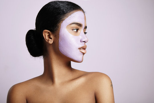 woman with a facial mask looks aside on a violet background