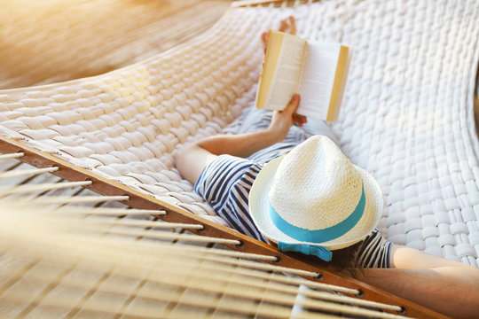 Man in hat in a hammock with book on a summer day