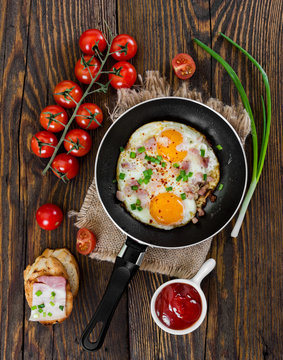 Fried eggs with ham and onion on wooden background.