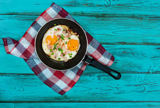 Fried eggs in pan on turquoise wooden background.
