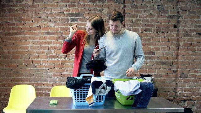 Young, happy couple listening to music on cellphone while folding clothes
