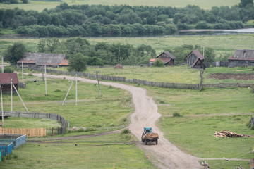 Tractor with wood moving through typical russian village by dirt