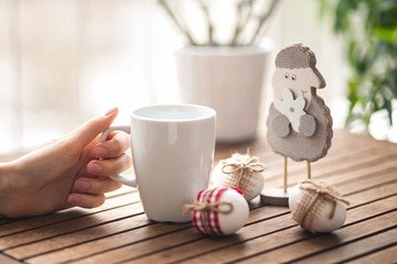 Woman's hands holding cup on table with wood sheep and easter eggs