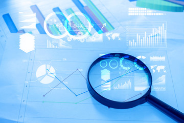 Magnifying glass and documents with analytics data lying on tabl