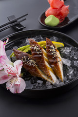 Eel sashimi with ice on a black plate with ginger wasabi over black background
