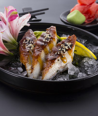 Eel sashimi with ice on a black plate with ginger wasabi over black background
