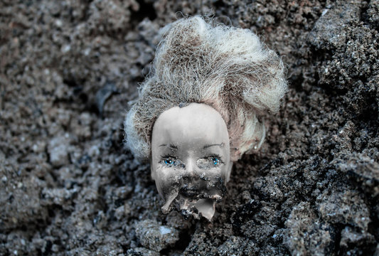 Plastic scald doll head lying in a pile of dirt