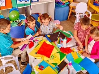 Group kids keeps colored paper on craft lesson in kindergarten .