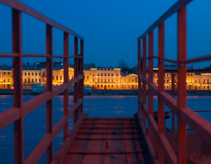 View of Neva and English embankment in St. Petersburg with night illumination through gangway on pier