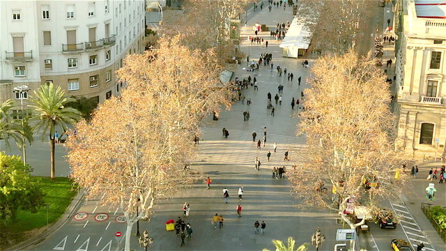 People walking on the streets of Barcelona. La Rambla famous street at end near sea.
