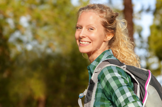 Hiking woman portrait smiling happy in forest. Female hiker girl trekking wearing backpack outside looking candid and fresh at camera. Beautiful young blonde girl living healthy lifestyle.