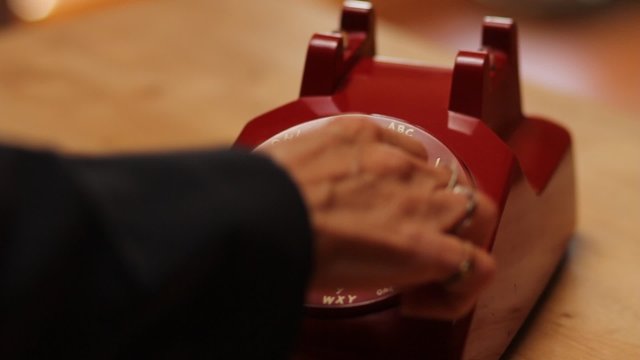 A woman frantically dials 911 on a vintage rotary phone