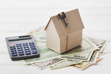 Model of cardboard house with key, calculator and cash dollars. House building, loan, real estate. Cost of public utilities, insurance, rent or buying a new home concept