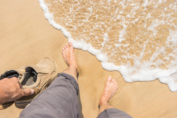 Male feet on the tropical beach sand, rolling wave