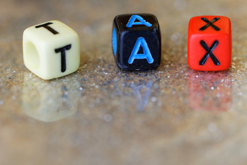 Close-up of alphabet block with TAX word on it. With glitter background and reflection of the word.