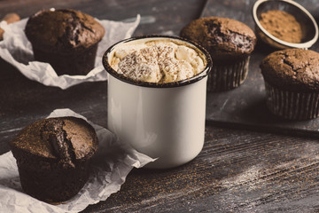 Cup of hot cocoa with marshmallows and chocolate muffins on the dark rustic wooden background. Toned image.