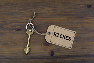 Key and a note on a wooden table with text - Riches