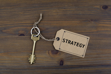 Key and a note on a wooden table with text - Strategy