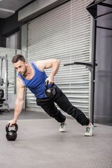 Obraz na płótnie Canvas Muscular man doing push up with kettlebells