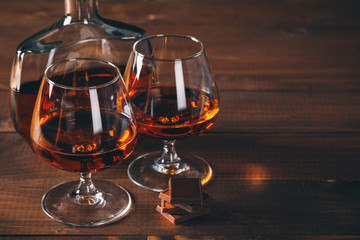 Two glasses of cognac and bottle on the wooden table. - obrazy, fototapety, plakaty