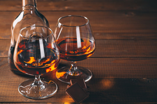 Two glasses of cognac and bottle on the wooden table.