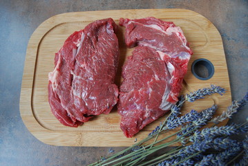 Fresh beef steak on a cutting board and lavender background.