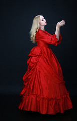 full length portrait of a beautiful blonde woman wearing a historical red silk, victorian era ball gown.