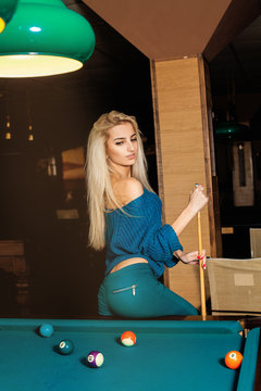 Vertical portrait of young fashionable girl posing on pool table