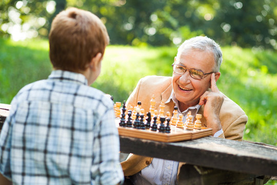 Grandfather and grandson are playing chess in park