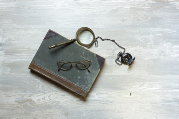 Old book with magnifier, reading glasses and pocket clocks