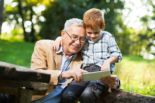 Grandfather and grandson are using digital tablet in park