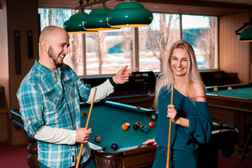 Horizontal portrait of smiling beautiful couple plays billiard