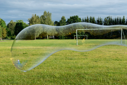 Big soap bubble, .green grass, trees, football ground and natural environment. Torma, small village in Estonia. Europe
