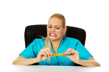 Shocked and scared female nurse or doctor sitting behind the desk and holding packet of pills