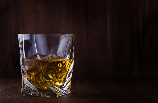 Glass of scotch whiskey and ice on a wooden background with copyspace