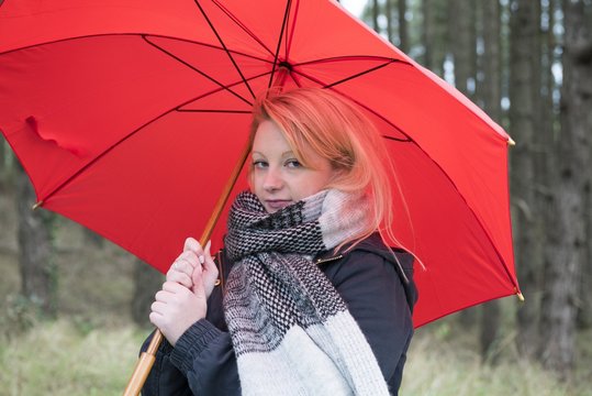 Portrait image of a young woman outdoors, on a rainy day with a red umbrella.