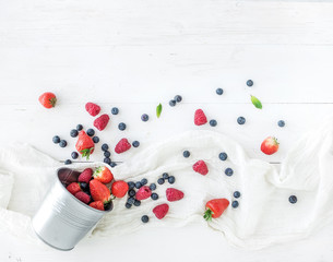 Berry frame with copy space on right. Metal bucket, strawberries, raspberries, blueberries and mint leaves, white wooden background, top view