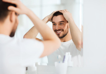 happy young man looking to mirror at home bathroom