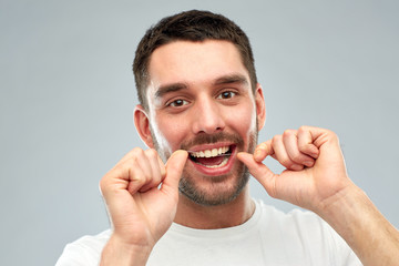 man with dental floss cleaning teeth over gray