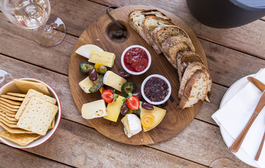 Wine tasting with delicious cheese platter on a wooden board, with figs, olives, strawberry, homemade jams, plain crackers and tasty bread.
