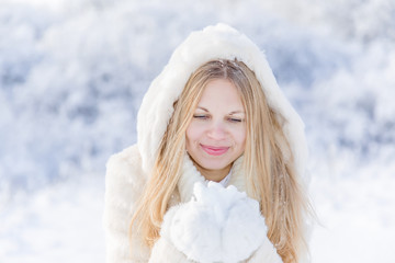 Smiling young blonde haired girl with snow in her hands in winter