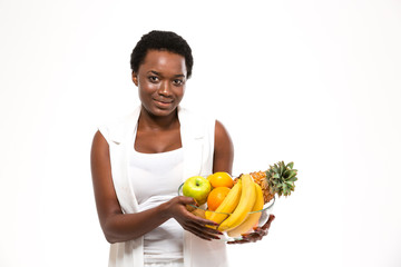 Obraz premium Beautiful cheerful african woman standing and holding exotic fruits
