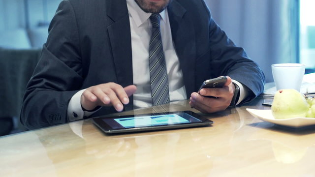 Businessman hands comparing data on tablet computer and smartphone by table at home
