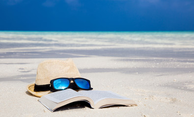 Hut mit Sonnenbrille und Buch am Strand