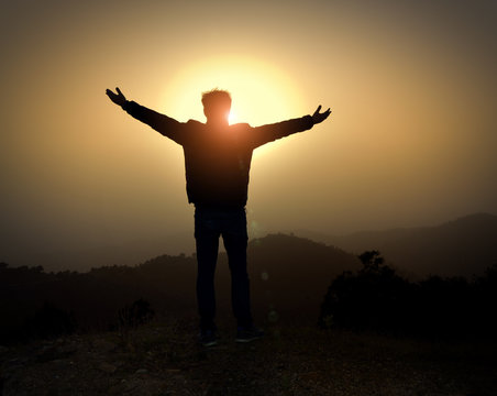 man with arms raised at sunset in the mountains 